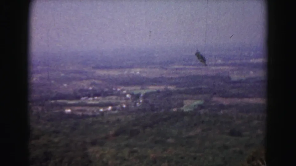 1963 Hagerstown-area landscape frame showing farmland, wooded terrain, haze, and a possible distant aircraft or film mark.