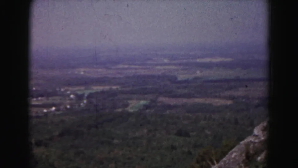 1963 Hagerstown-area home-movie frame looking over a wooded valley toward hazy farmland, with rock in the foreground.
