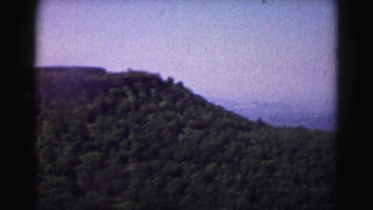 Forested mountain ridge under a hazy purple sky with dark 8mm frame edges.
