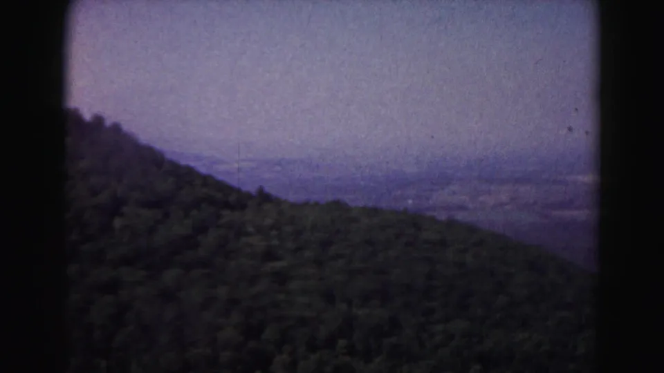 1963 8mm frame of a forested slope near Hagerstown with a hazy rural valley beyond.