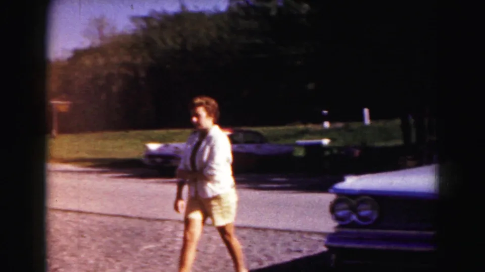 Young man in light clothing walks past parked cars in 1963 Hagerstown, Maryland travel footage.