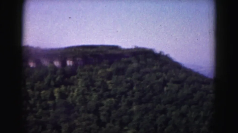 Wide 1963 home-movie view of wooded hills and pale sky, likely from the road-trip sequence.