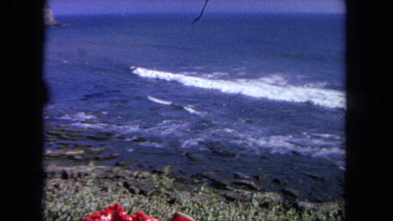 Rough ocean waves breaking over a rocky shoreline, framed by dark film borders.