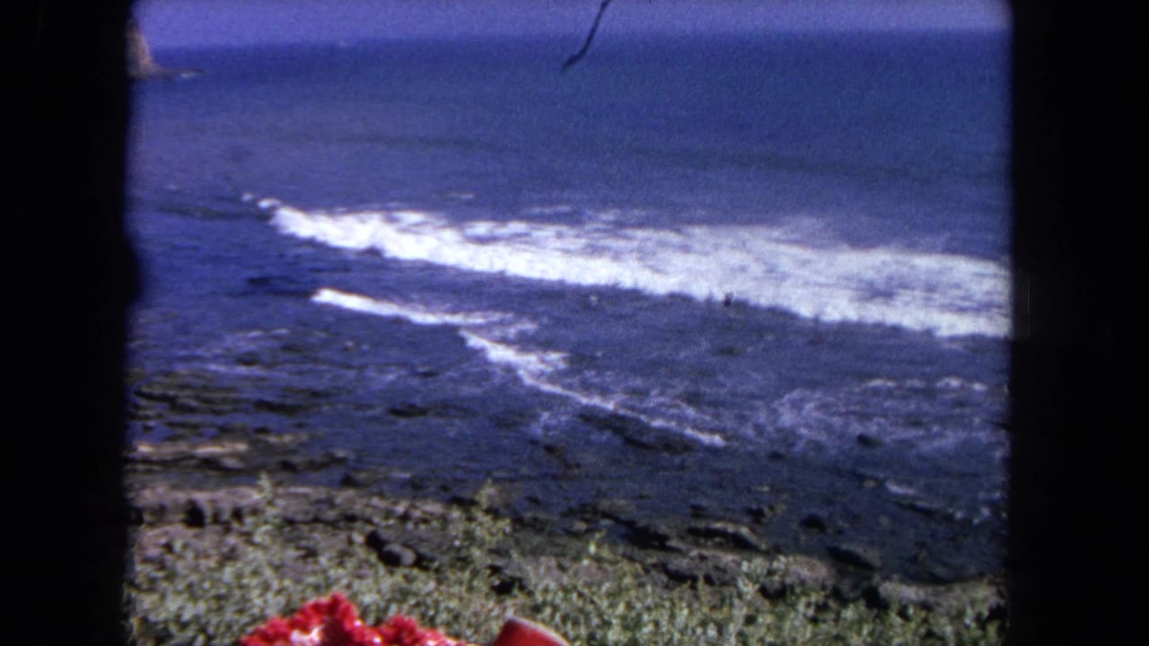 Ocean surf rolling toward a rocky shore with dark borders on the frame.