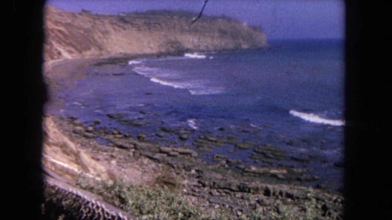 1962 Tijuana shoreline footage showing a cliff face, rocky beach, and white surf lines across saturated blue water.