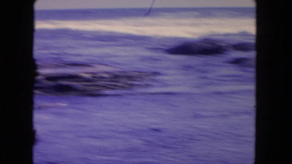 Motion-blurred 8mm view of Tijuana shoreline water, with surf streaks and dark rocks softened by camera movement.