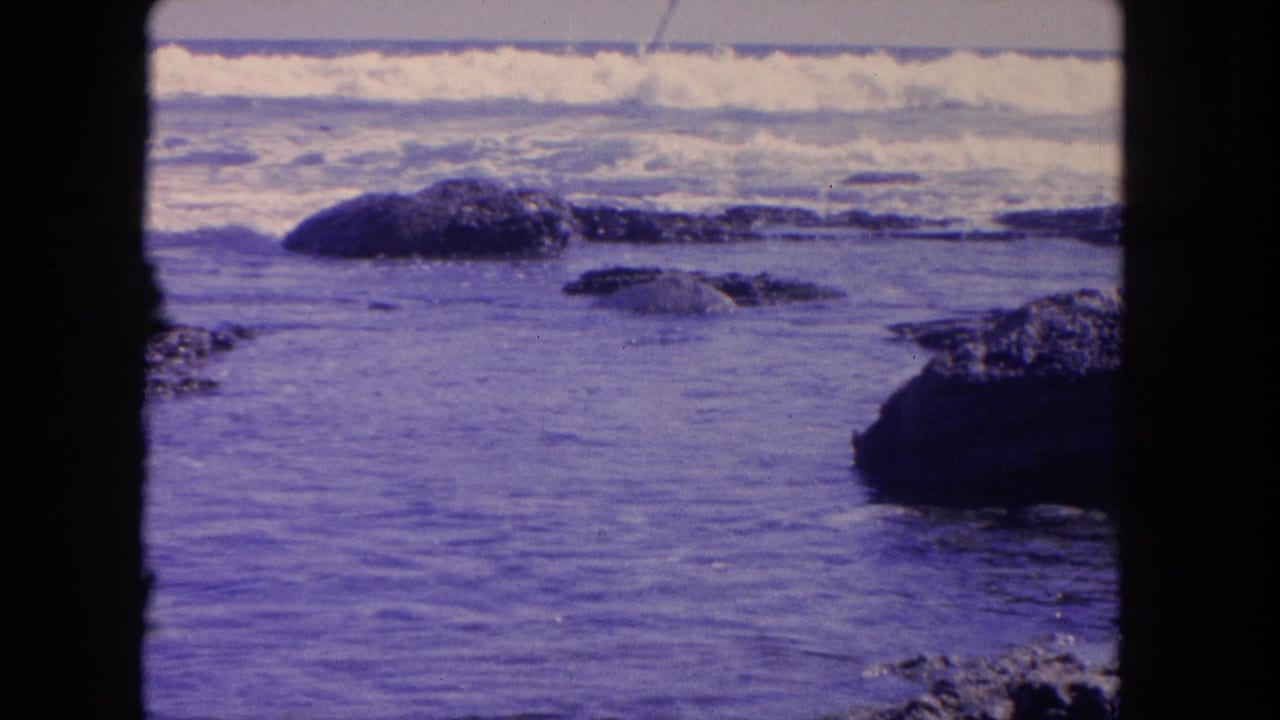 Rocky shoreline with low waves and white surf across the top of the frame.