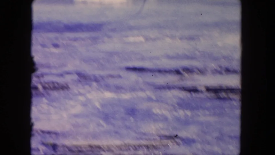 1962 Tijuana 8mm frame with motion-softened surf moving over dark coastal rocks, bordered by the film gate edges.