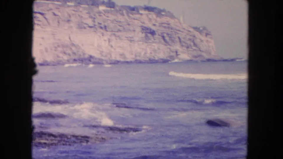 1962 Mexico travel footage shows waves breaking along a rocky shoreline below a pale coastal cliff.