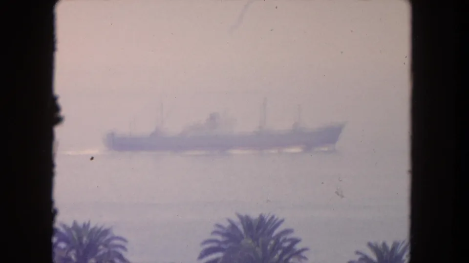 1962 Tijuana-area 8mm frame with a larger ship silhouette softened by haze above palm trees and the coastline.