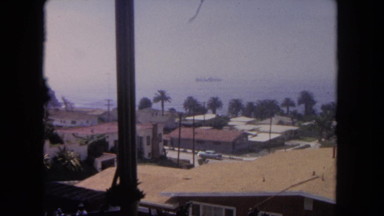 A steady 1962 Tijuana window view shows sunlit rooftops, palm trees, ocean haze, and a distant large ship on the water.