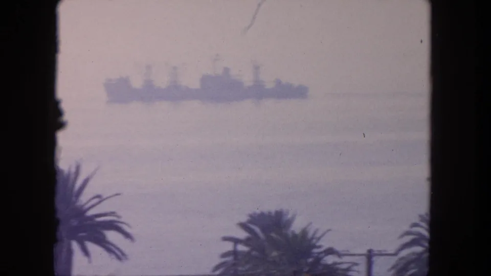 A 1962 Tijuana coastal shot centers on a large hazy ship offshore, with dark palm silhouettes and a utility pole below.