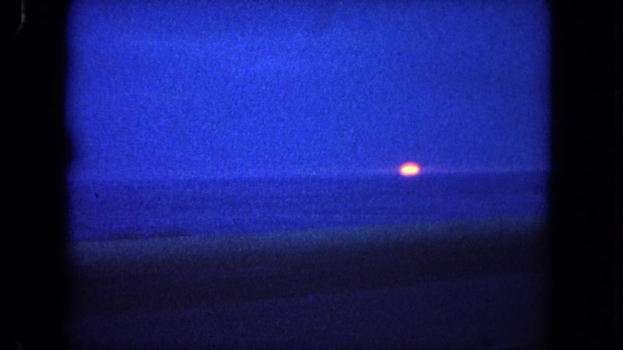 Deep blue ocean sunset with a small orange sun near the horizon.