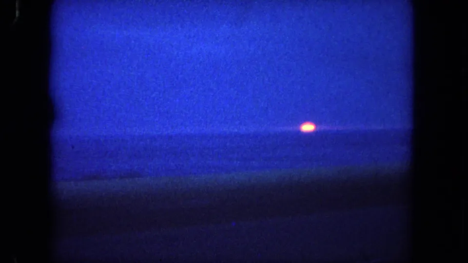 1962 8mm home-movie frame of a deep blue ocean horizon near Tijuana, Mexico, with a small orange sun setting over the water.