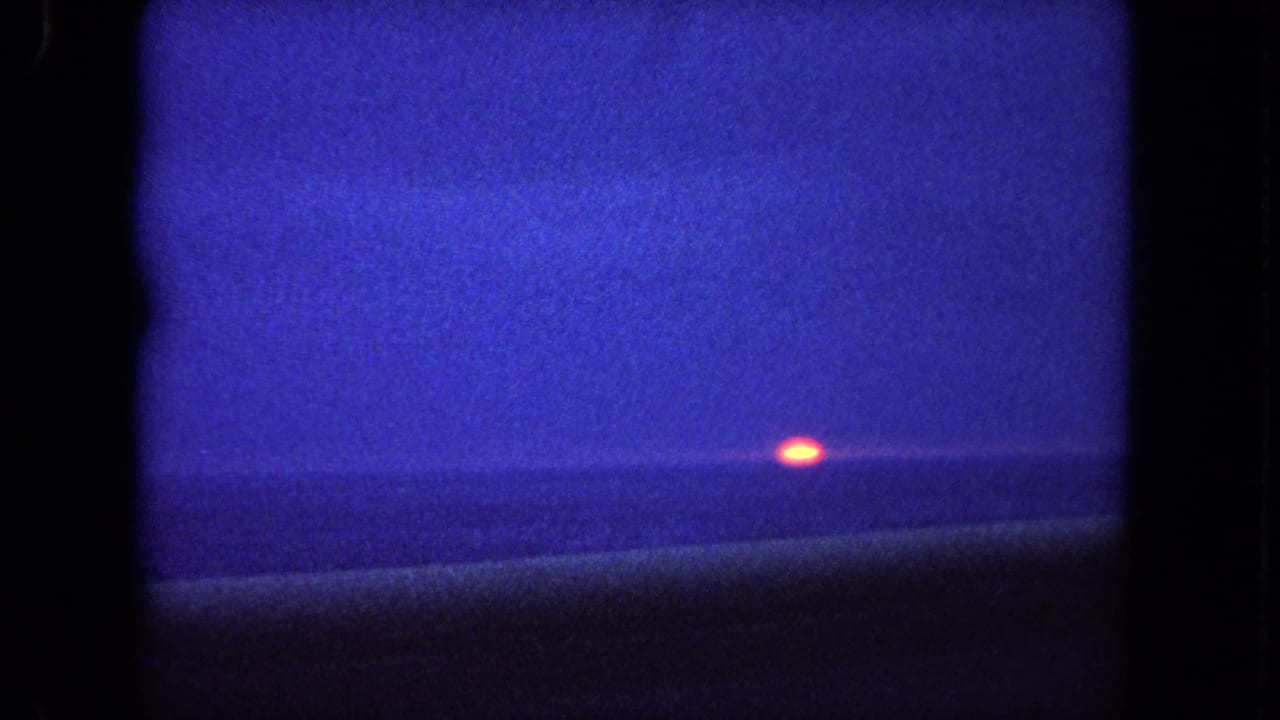 1962 Tijuana, Mexico 8mm frame showing a small orange sun just above a blue ocean horizon at dusk.