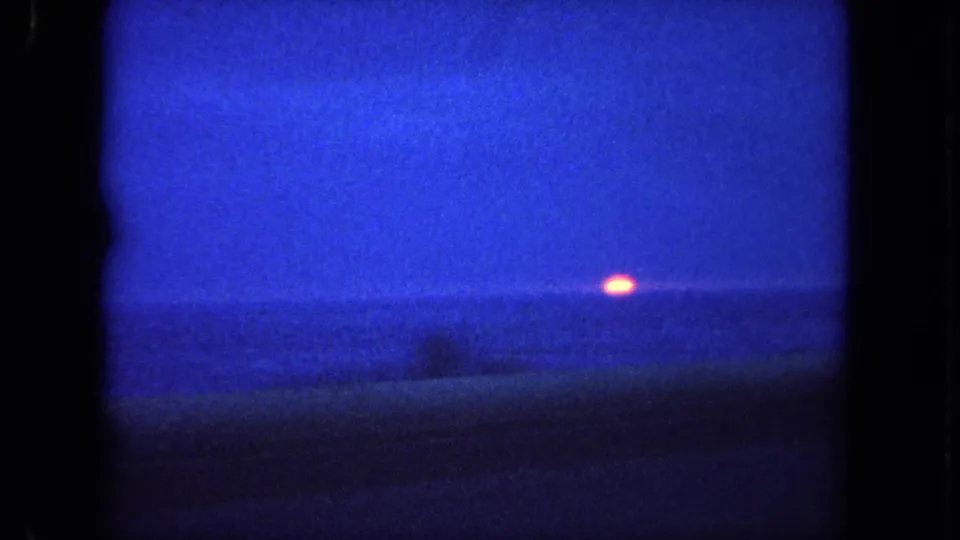 1962 Tijuana, Mexico travel-film frame showing the sun near the ocean horizon under a blue dusk sky.