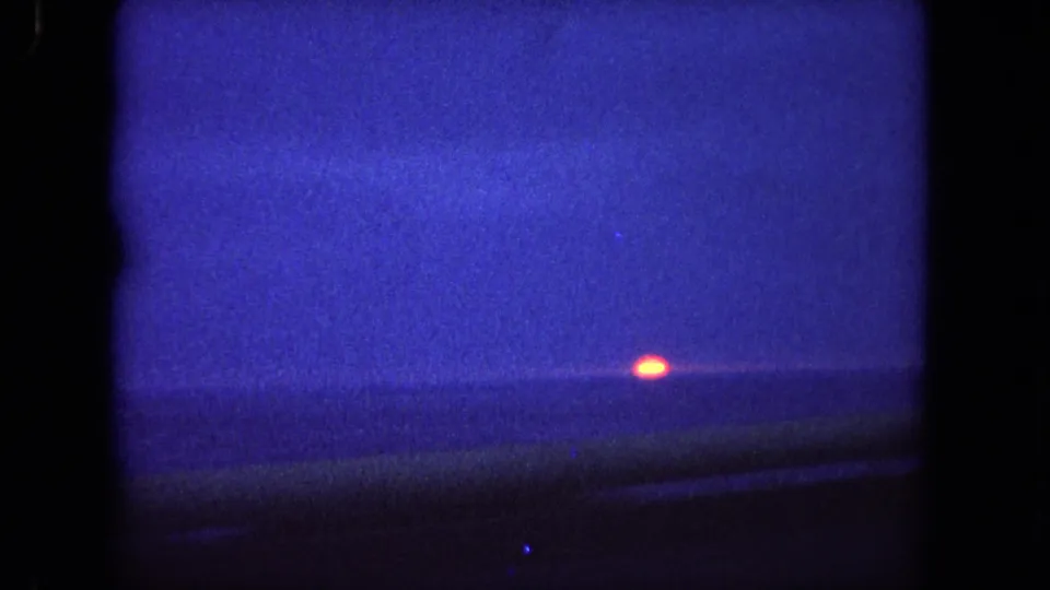 A 1962 coastal sunset view near Tijuana, showing the orange sun close to the ocean horizon with dark foreground blur from the car.