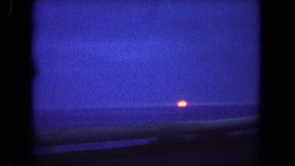 End-frame coastal sunset near Tijuana, with the orange sun low over the ocean and heavy blue 8mm color shift around the window-framed view.