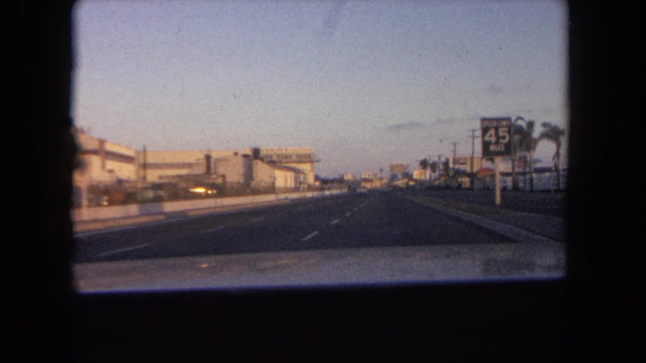 1962 Tijuana driving shot with a 45 speed sign, commercial roadside structures, palms, and dusk light ahead.