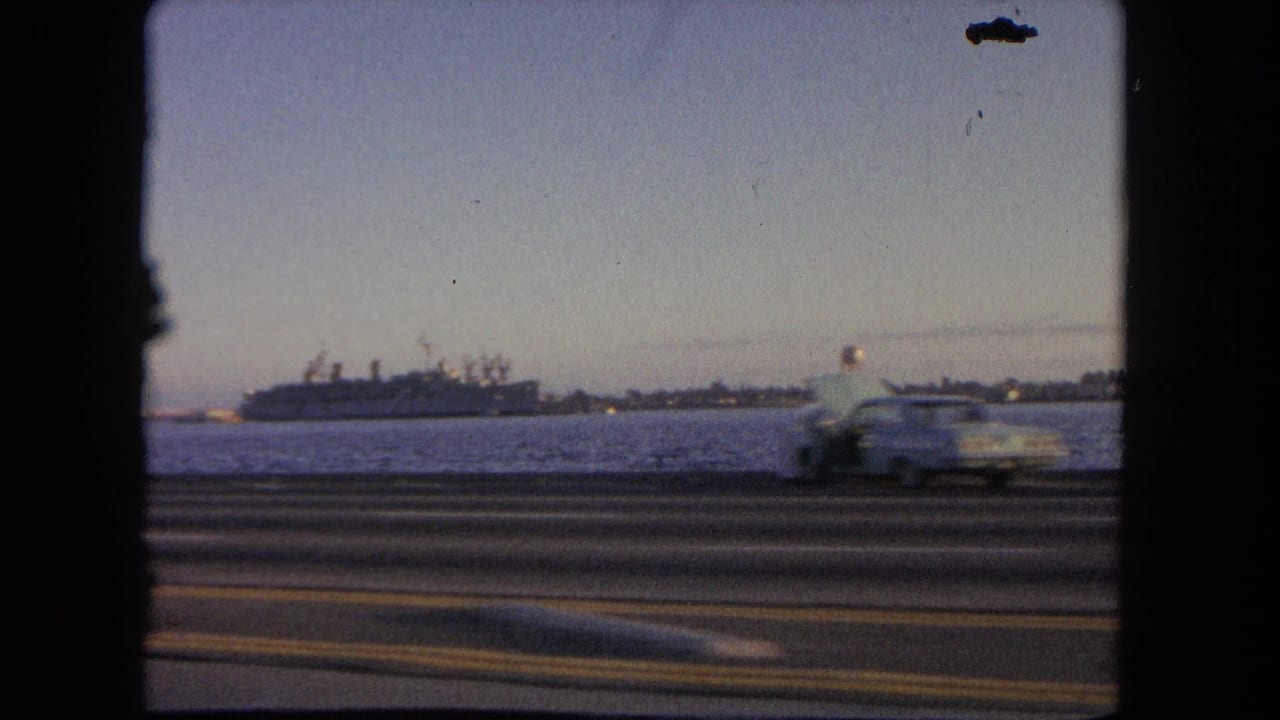 1962 Tijuana home-movie view from a moving vehicle, showing a docked ship across water and a car passing on the highway.