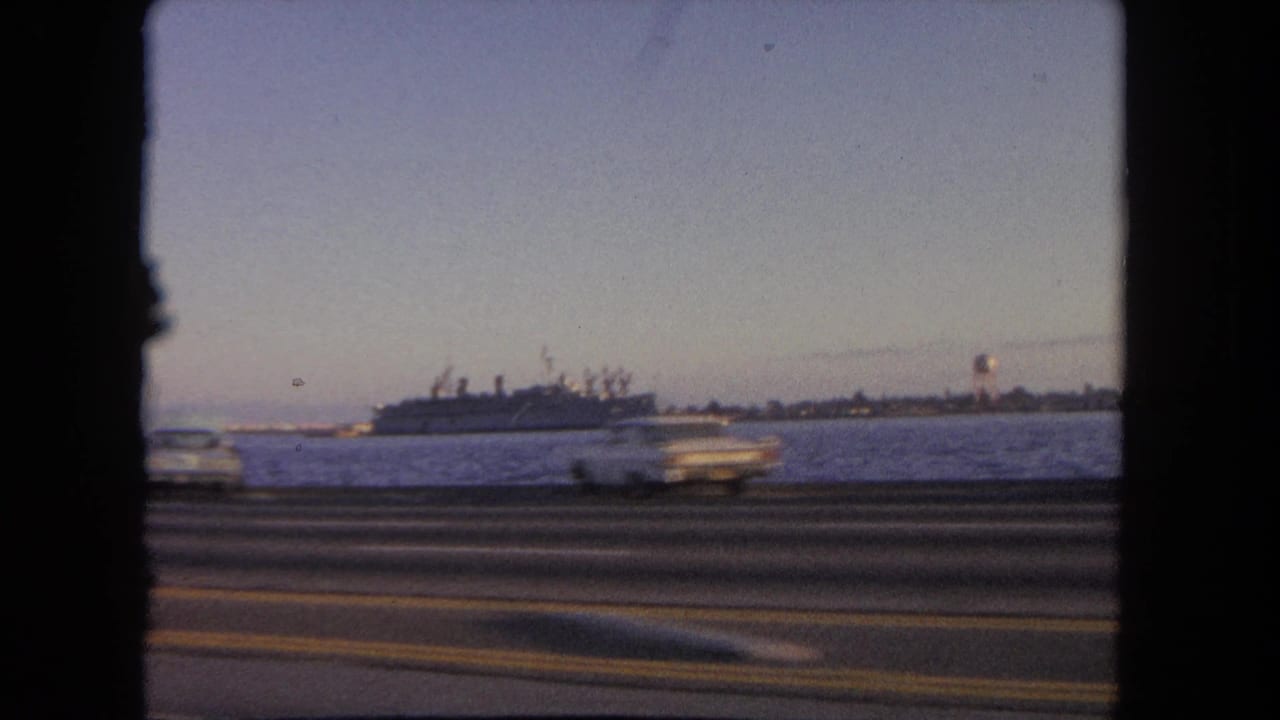 Harbor water, distant ship, shoreline water tower, and blurred cars on the road.