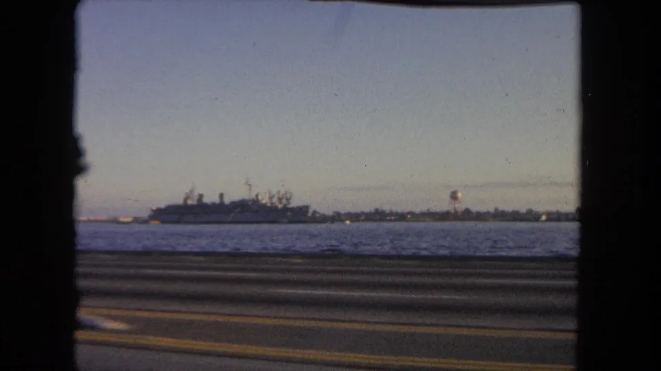 1962 Tijuana coastal road footage showing water, a large naval ship, and a distant round tower-like structure on the shoreline.