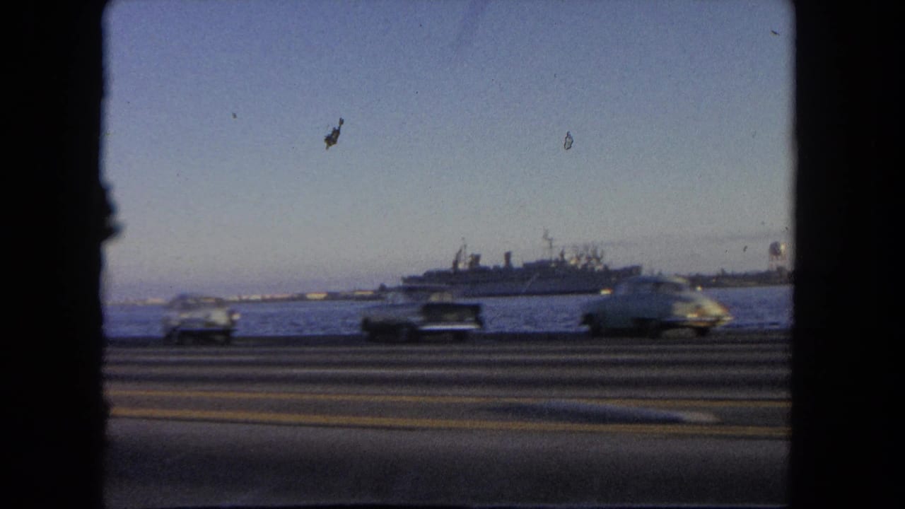 Passing cars on a road with open water and a large ship in the distance.