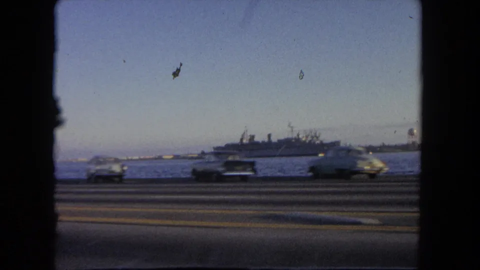 1962 Tijuana driving view with blurred cars crossing the foreground and a large ship visible across the water.