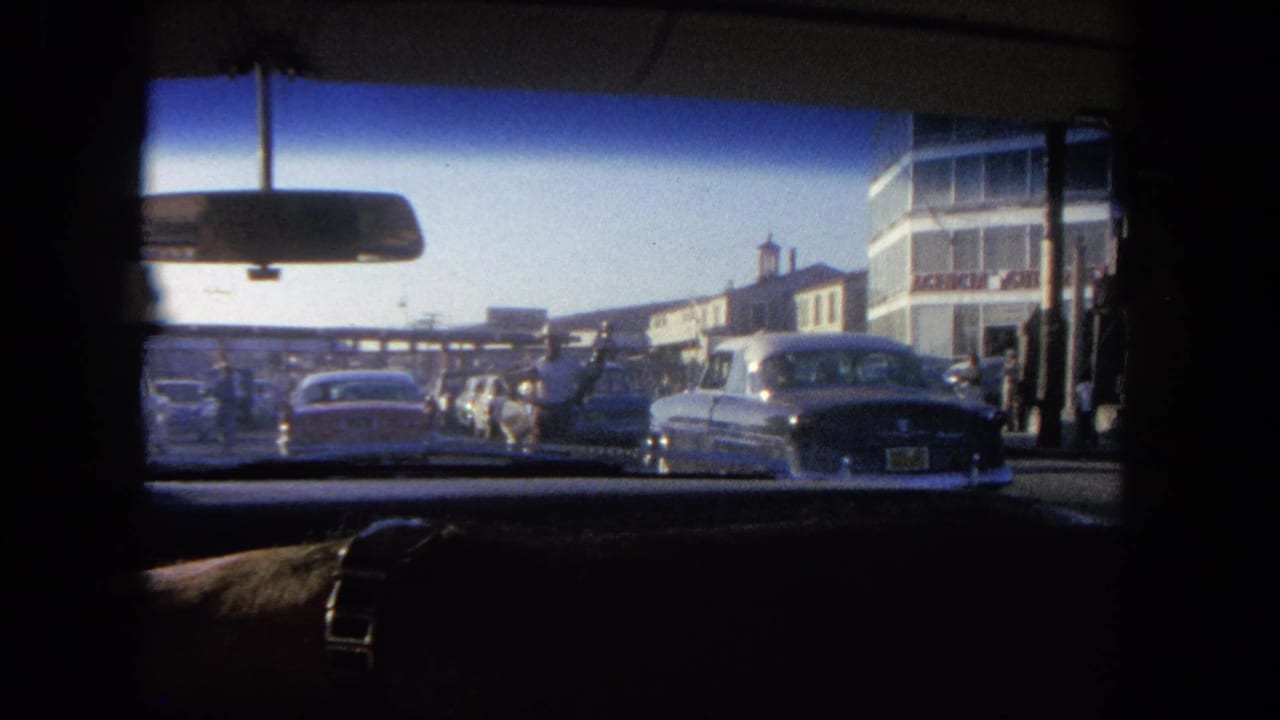 1962 Tijuana home-movie view from inside a car, looking through the windshield at vehicles queued near a toll plaza.