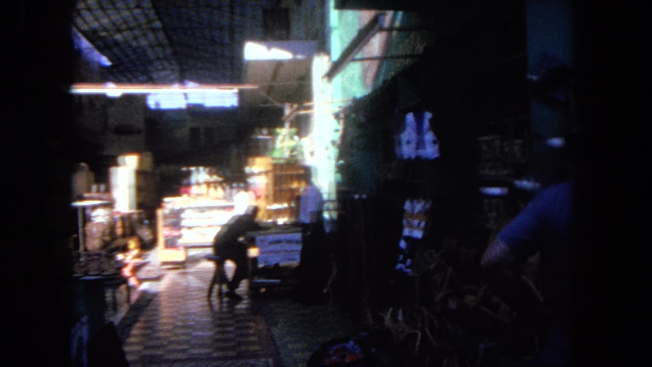Late in the clip, the Tijuana market aisle shows a seated adult, illuminated display cases, hanging merchandise, and deep interior shadows.