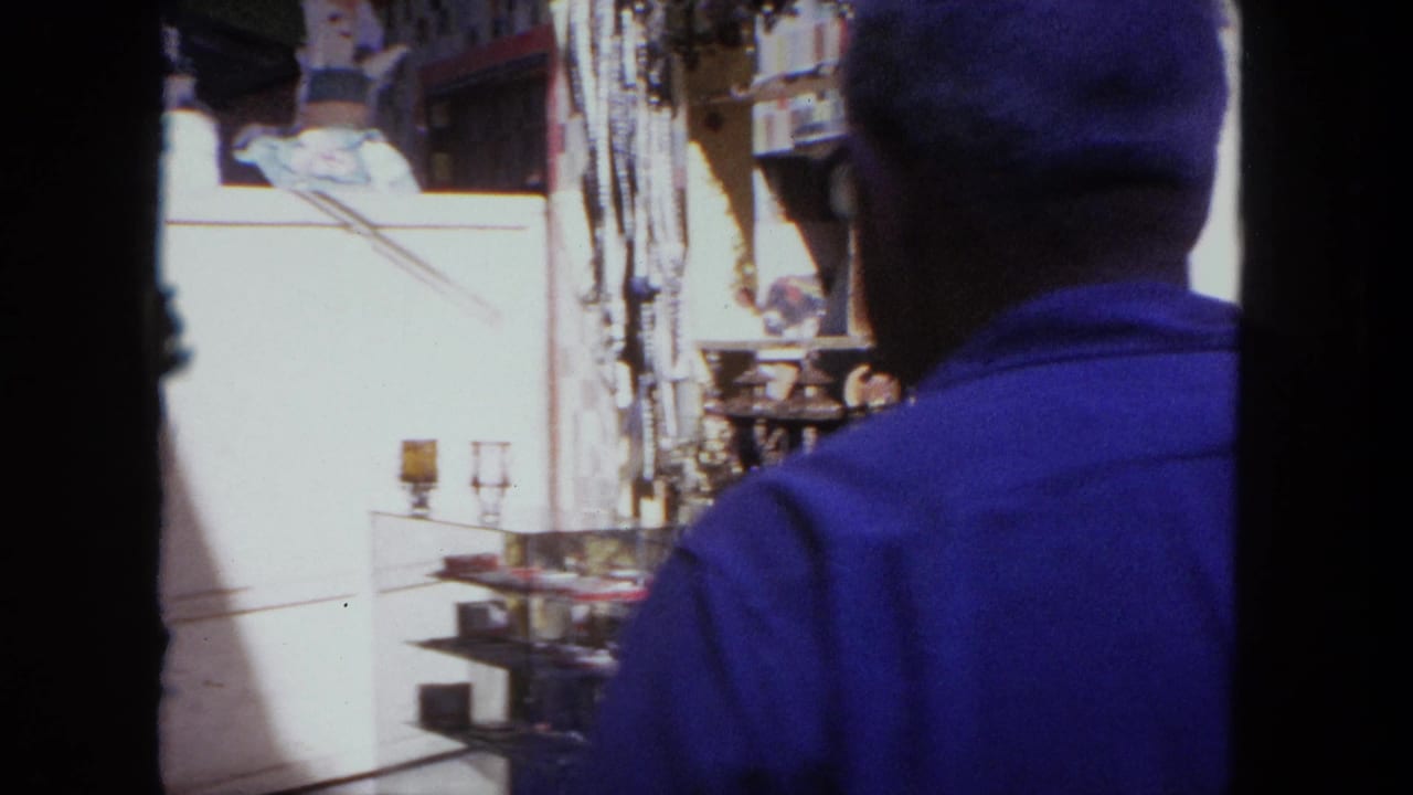 Man in a blue shirt seen from behind near market stalls and glass display shelves.