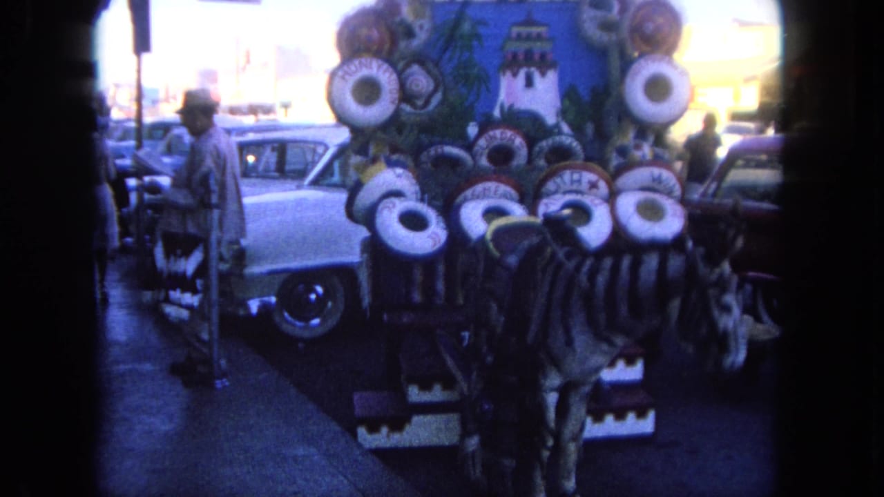 Painted zebra display near a curb with classic cars and pedestrians in the background.