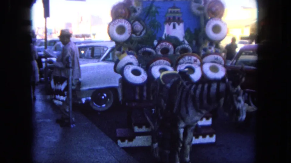 1962 Tijuana street view with a painted zebra-like display, rounded classic cars, and pedestrians near the curb.