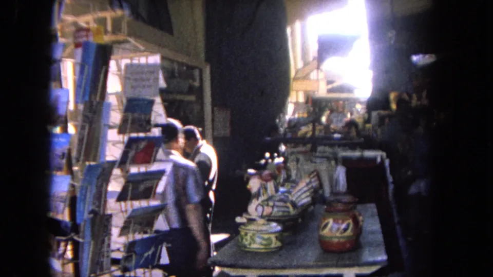 Tijuana shop or market interior with shelves, counter displays, painted goods, and visitors moving through bright doorway light.