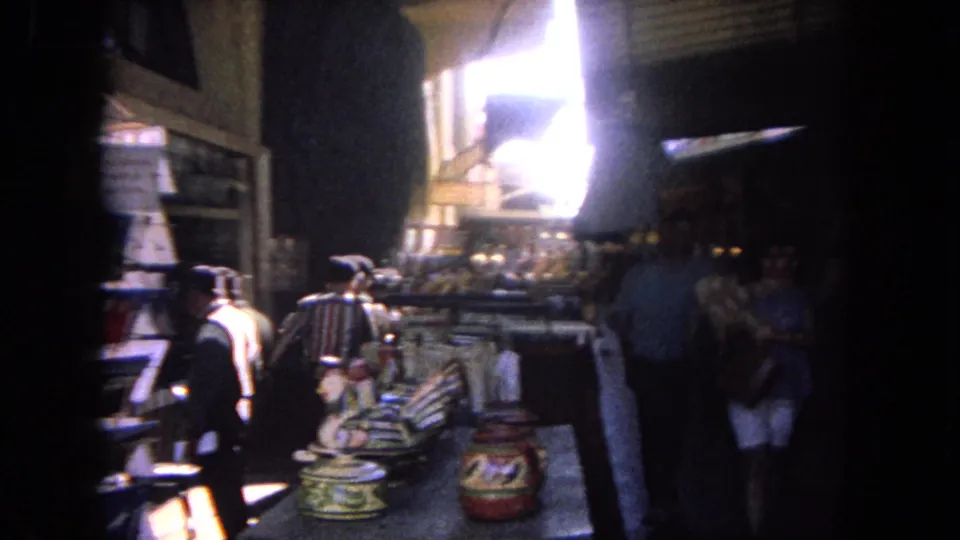 1962 Tijuana market interior view with counters of goods, shelving, several adults, and strong daylight at the entrance.