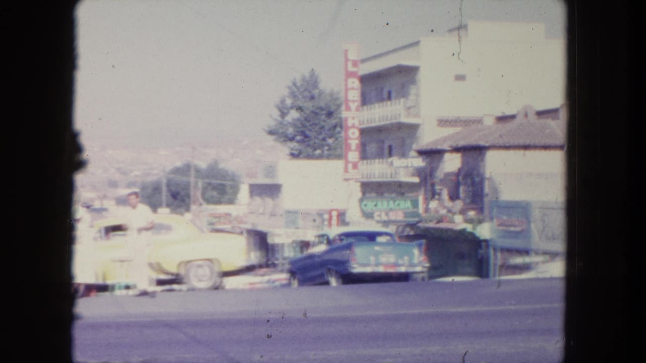 Hotel sign, parked cars, and pedestrians on a sloped street.