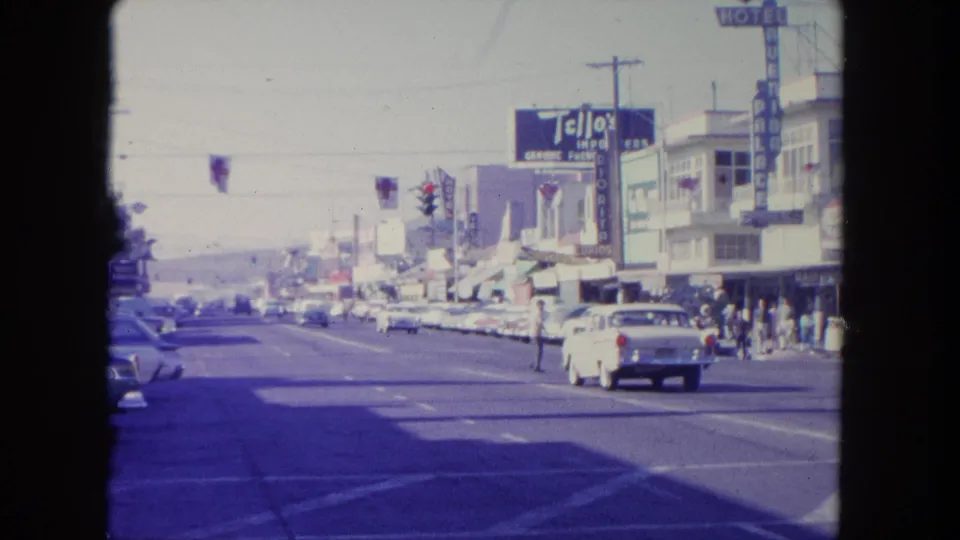 1962 Tijuana street footage shows cars passing a crosswalk beneath traffic lights, with Tello's and other storefront signs visible.