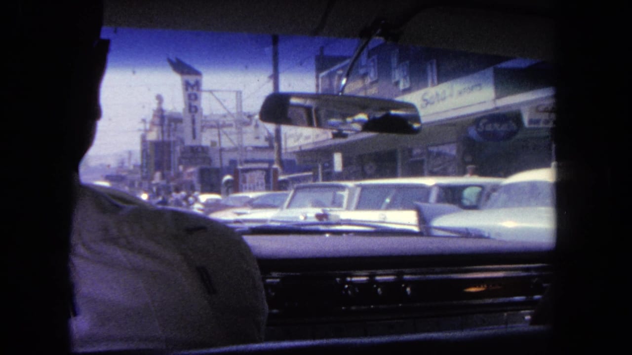 View through a car windshield toward parked cars, storefronts, and a Mobil sign on a busy street.