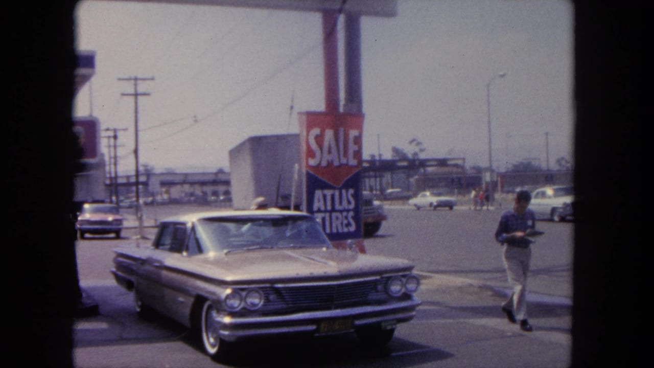 Parked silver sedan near a red sale sign as a man walks along the roadway.