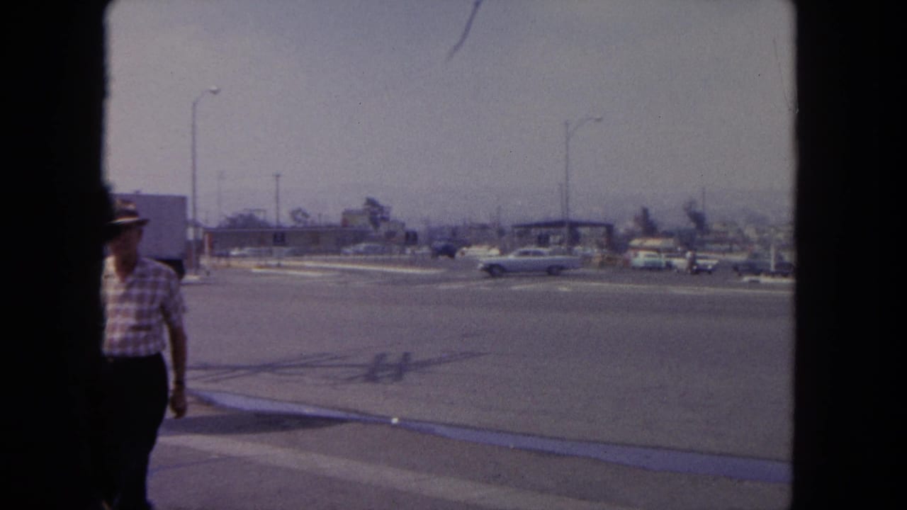 Wide street corner with classic cars, streetlights, low buildings, and a partly visible pedestrian.