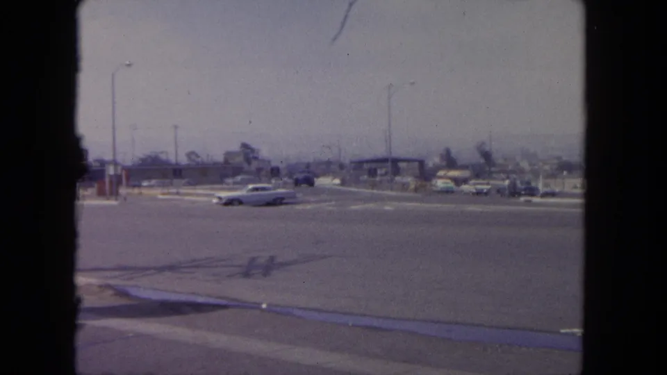 1962 Tijuana street scene showing early-1960s cars moving through a broad intersection with low commercial buildings in the background.