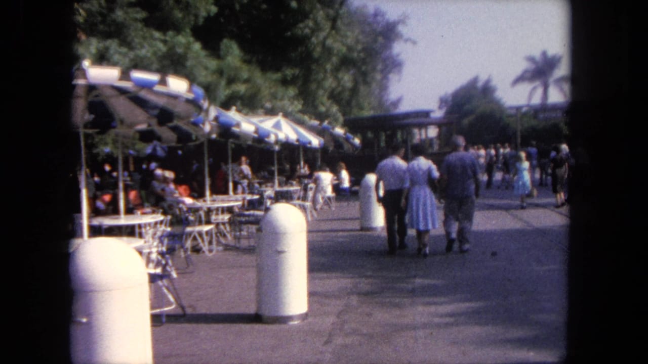 1962 Tijuana travel footage showing pedestrians on a sunny walkway beside blue-and-white umbrellas and outdoor tables.