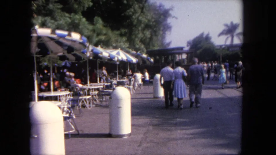 1962 Tijuana travel footage showing pedestrians on a sunny walkway beside blue-and-white umbrellas and outdoor tables.
