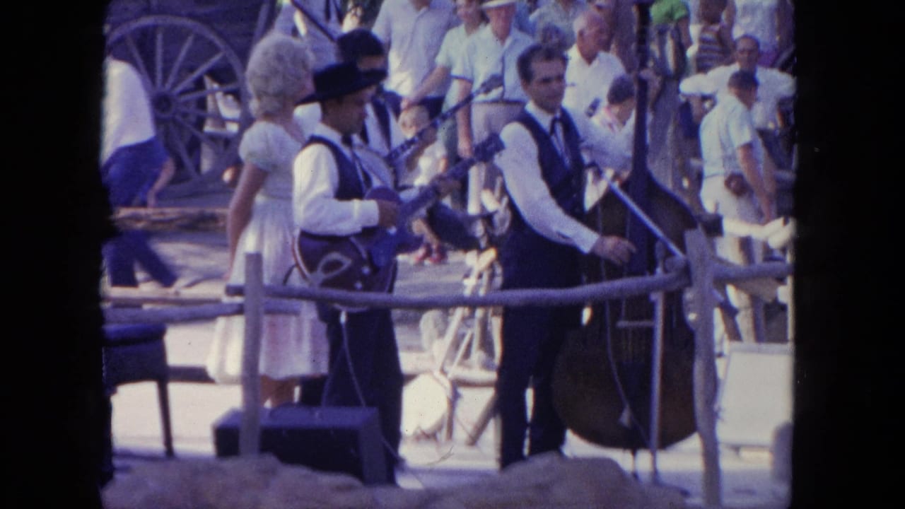 Two musicians play guitar and upright bass on an outdoor stage before spectators.