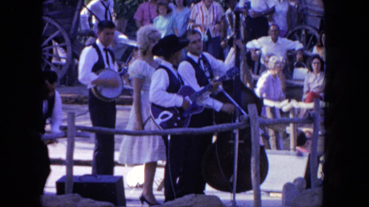 In 1962 Tijuana footage, musicians in white shirts, dark vests, and cowboy hats perform while spectators watch behind them.