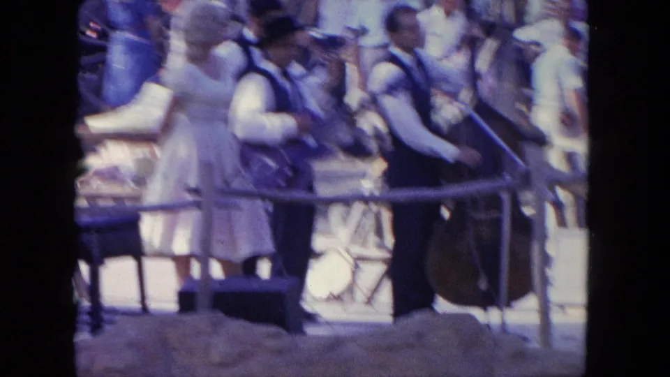 A soft, motion-blurred 1962 Tijuana frame shows the country-style performers shifting positions on the outdoor stage.