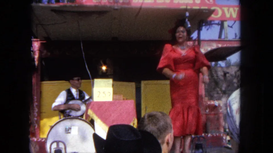 The singer faces the audience on the 1962 Tijuana carnival stage, with a 25-cent placard and banjo player visible nearby.