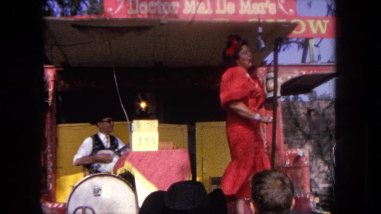 Performer in red stands near a microphone while a musician plays beside a drum.