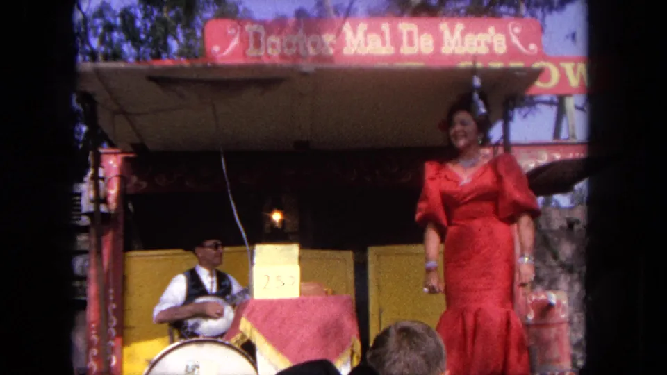 The red-dressed singer smiles at the front of the Tijuana stage as the seated musician remains behind her near the drum and 25 cent sign.