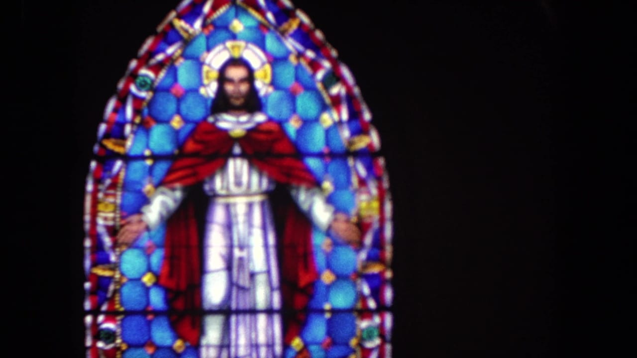 Stained glass figure of Jesus with arms outstretched in a blue and red altar window.